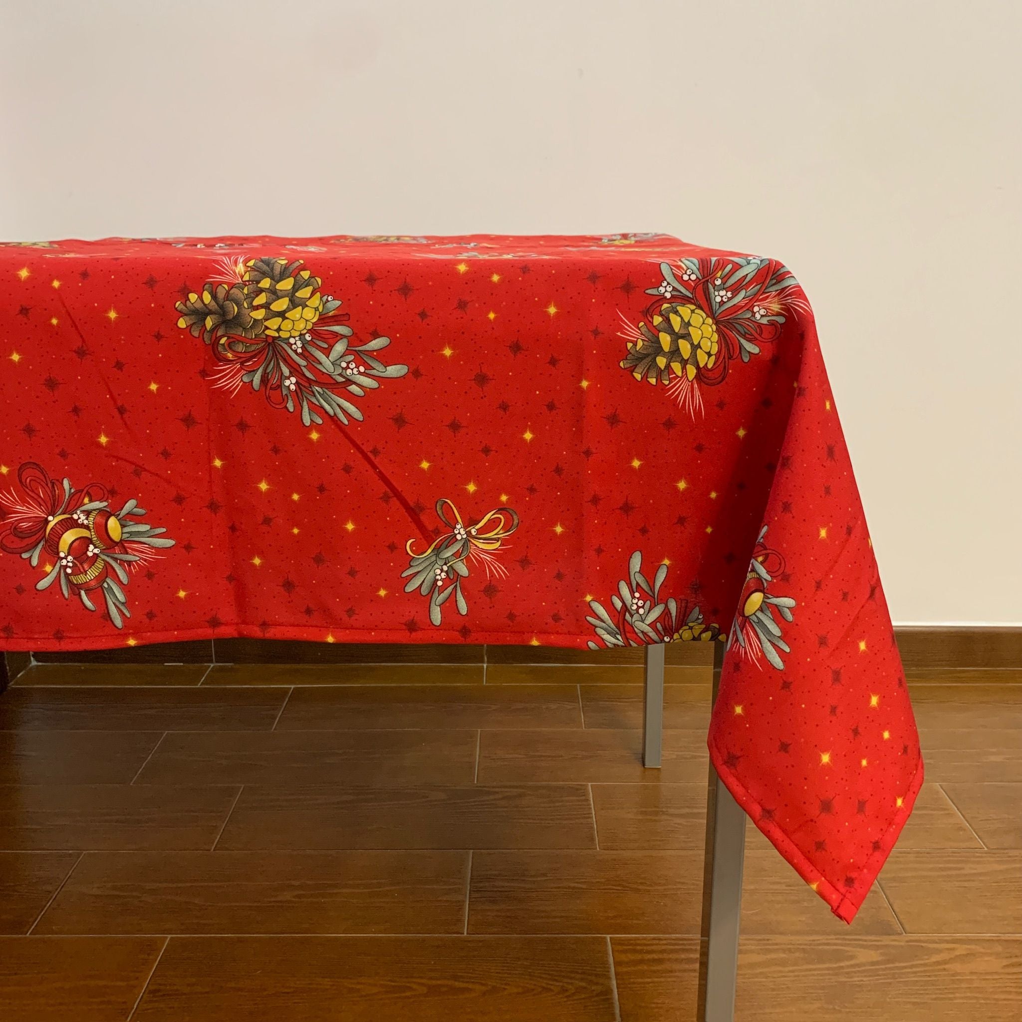 A Toalha de Mesa Natal Bolas é uma toalha festiva cujo fundo é vermelho, e está repleta de bolas de natal às riscas vermelhas e douradas, e pinhos natalícios entrelançados em pequenos laços.