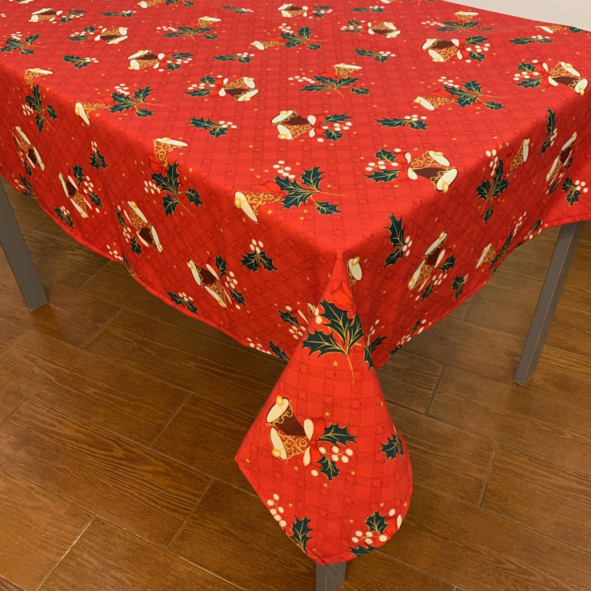 Toalha de Natal vermelha composta um arranjo de 2 sininhos feito por um laço vermelho enfeitado por duas pequenas folhas de azevinhos.